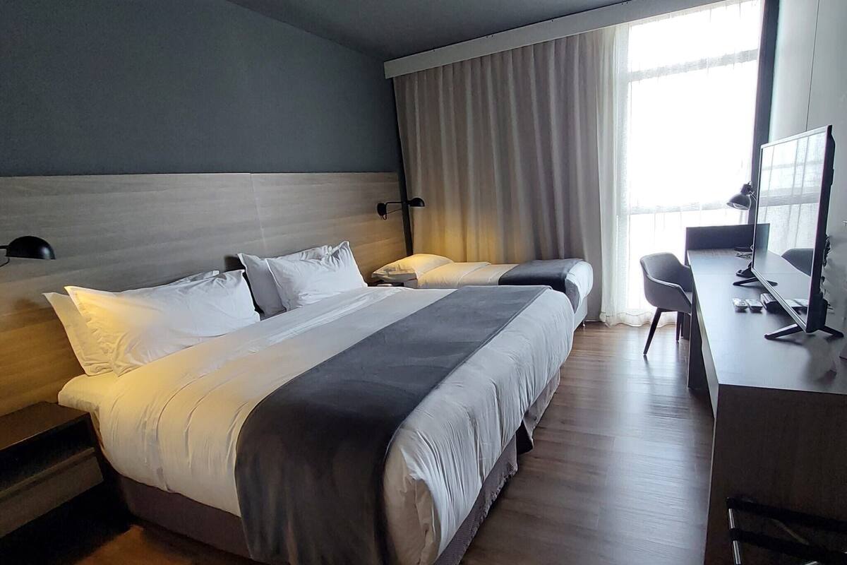 Une chambre d’hôtel moderne avec un grand lit, un bureau équipé d’un ordinateur et une fenêtre avec des rideaux.