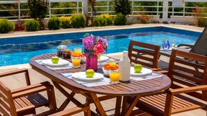 Una mesa de madera dispuesta con platos, vasos y un florero junto a una piscina.