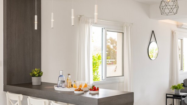 A modern kitchen with a central island, white bar stools, pendant lighting, and a view to the outside. - Napa Bay View Villa 4 (Ayia Napa)