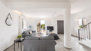 A modern living room with a grey sofa, a small table with a plant, a TV, and a staircase. - Napa Bay View Villa 4 (Ayia Napa)