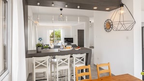 A modern kitchen with a dark countertop, white chairs, and pendant lighting. - Napa Bay View Villa 4 (Ayia Napa)