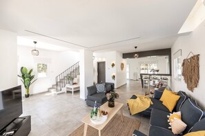 Uma sala de estar espaçosa, com sofá, mesa de centro e televisão. Uma escada leva a outro cômodo.