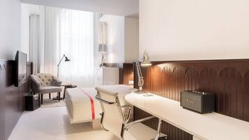 Ein Hotelzimmer mit Bett, Schreibtisch, Stuhl, Lampe, Radio und Koffer.