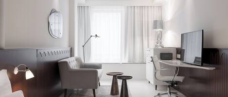 A hotel room with a bed, a desk, a chair, a TV, and a window with curtains.