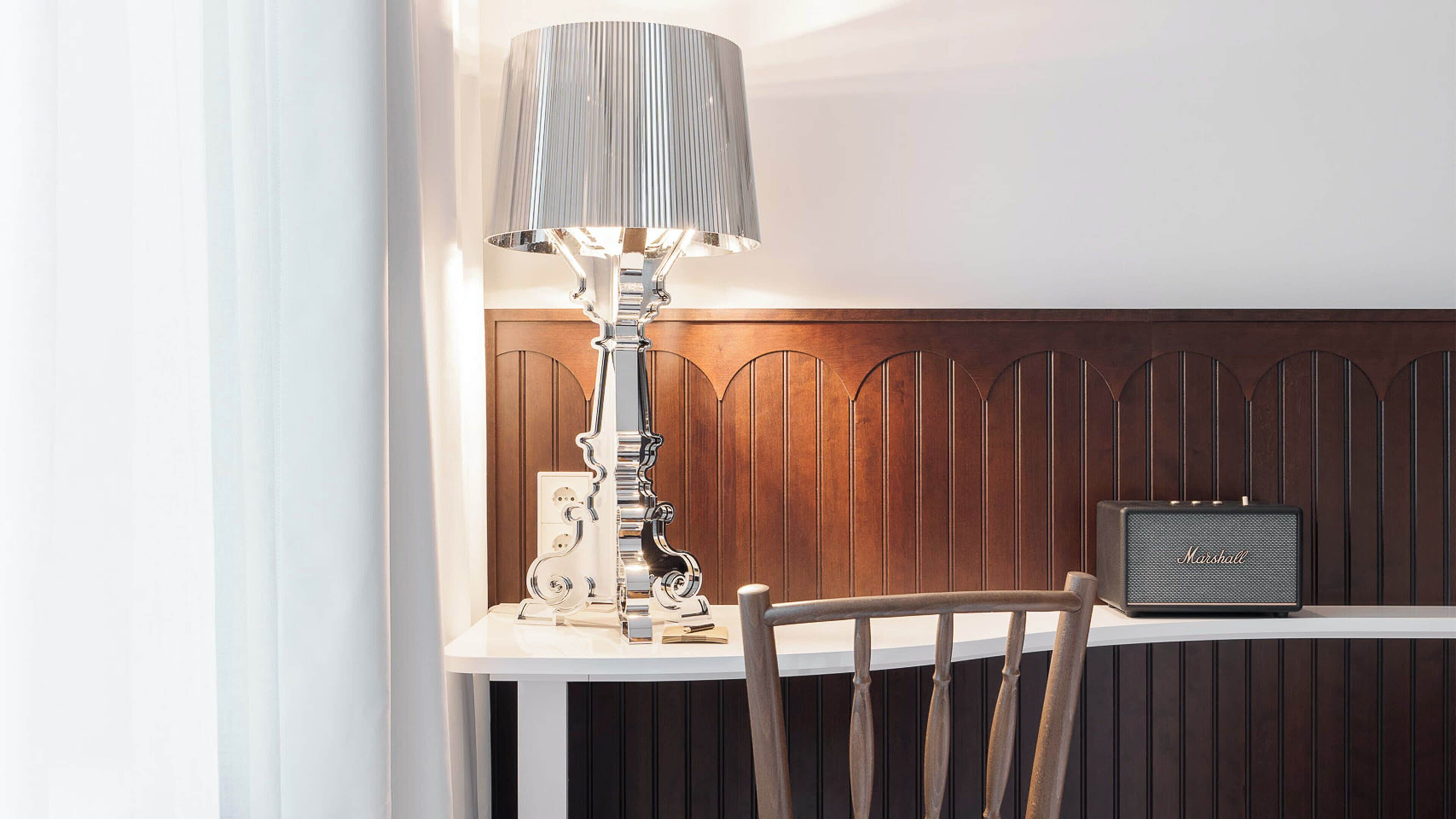 A table with a lamp, a radio, and a chair in a room with wooden paneling.