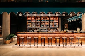 A bar with a long counter, multiple stools, and a well-stocked shelf of bottles.