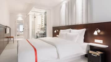 A modern hotel room with a large bed, a vanity with mirrors, a Marshall amplifier, and a walk-in closet.