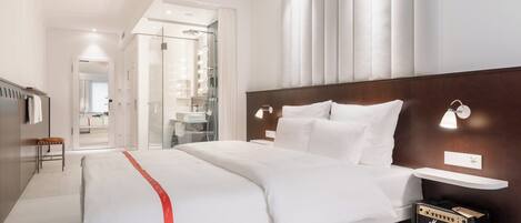 A modern hotel room with a large bed, a vanity with mirrors, a Marshall amplifier, and a walk-in closet.