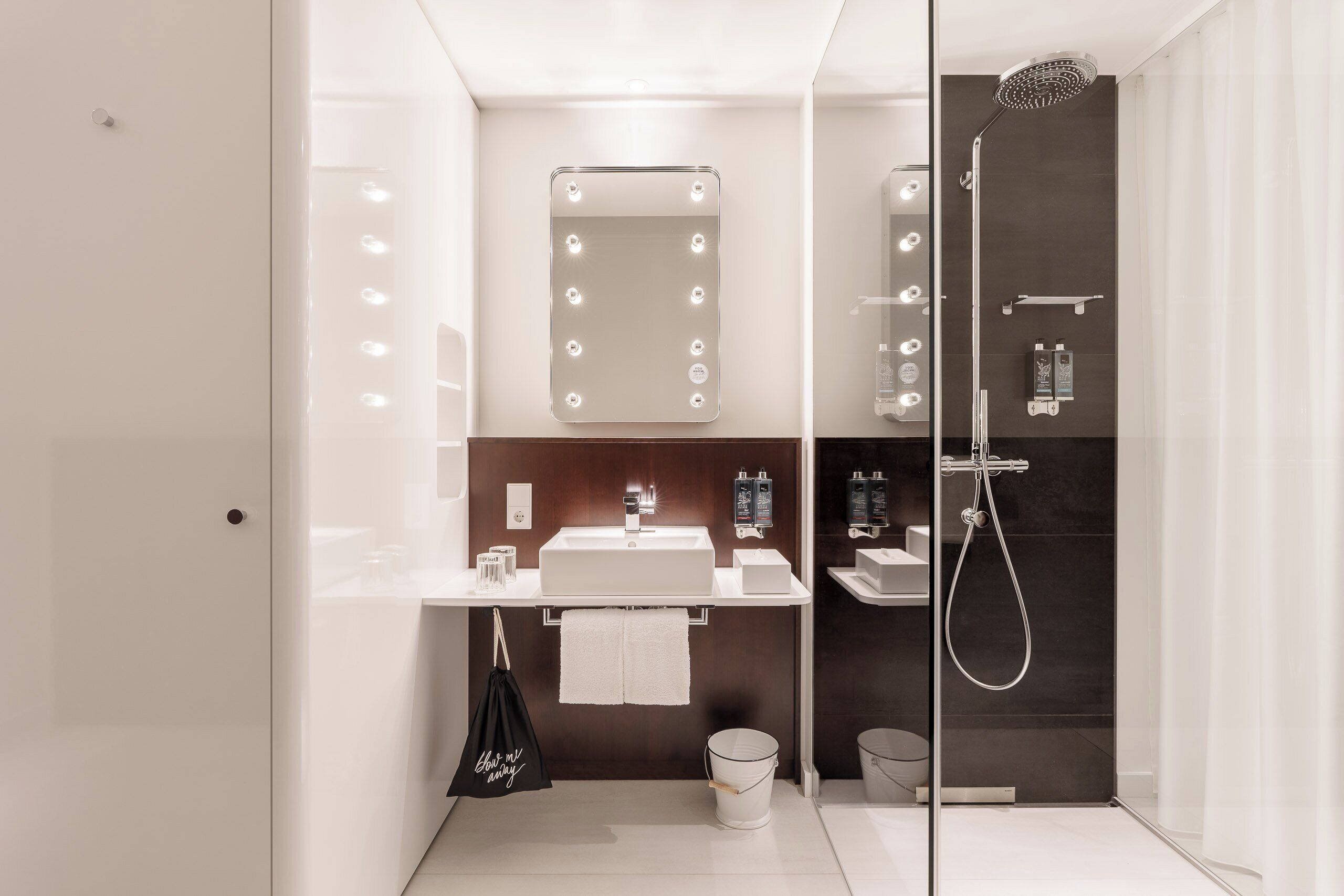 A modern bathroom with a vanity, mirror with lights, shower, and a glass partition.