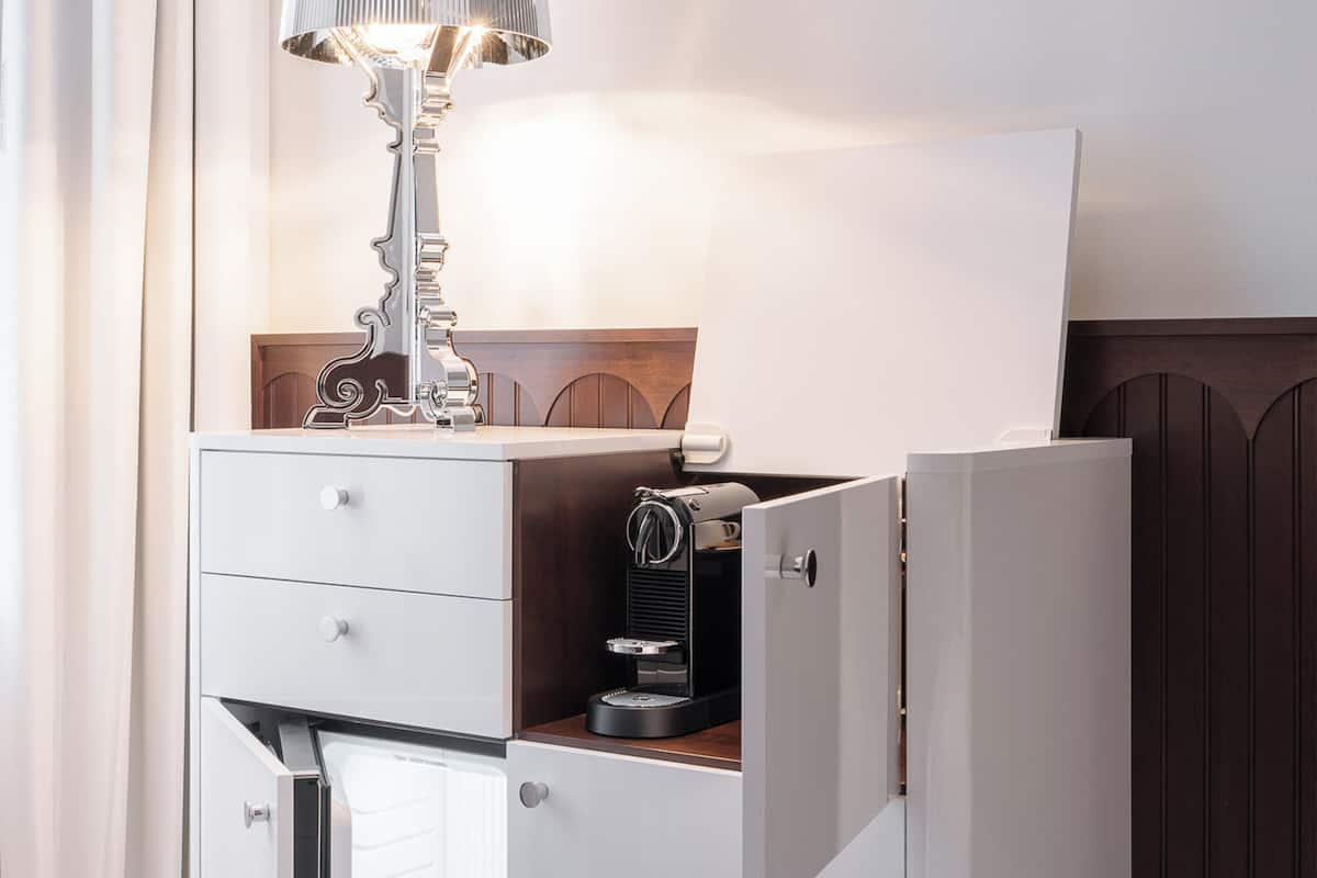 Un minibar moderno y compacto con una lámpara, una máquina de café y un enfriador de vino.