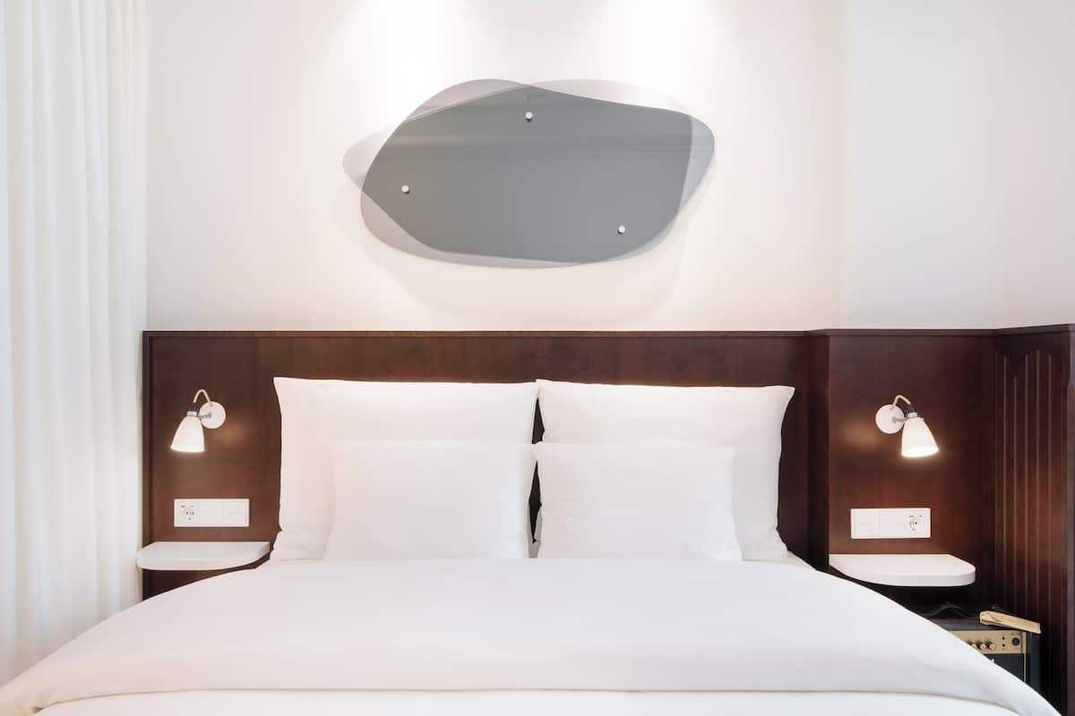 Una habitación de hotel moderna con cabecera de madera, dos mesitas de noche con lámparas y una cama grande con ropa blanca de cama.