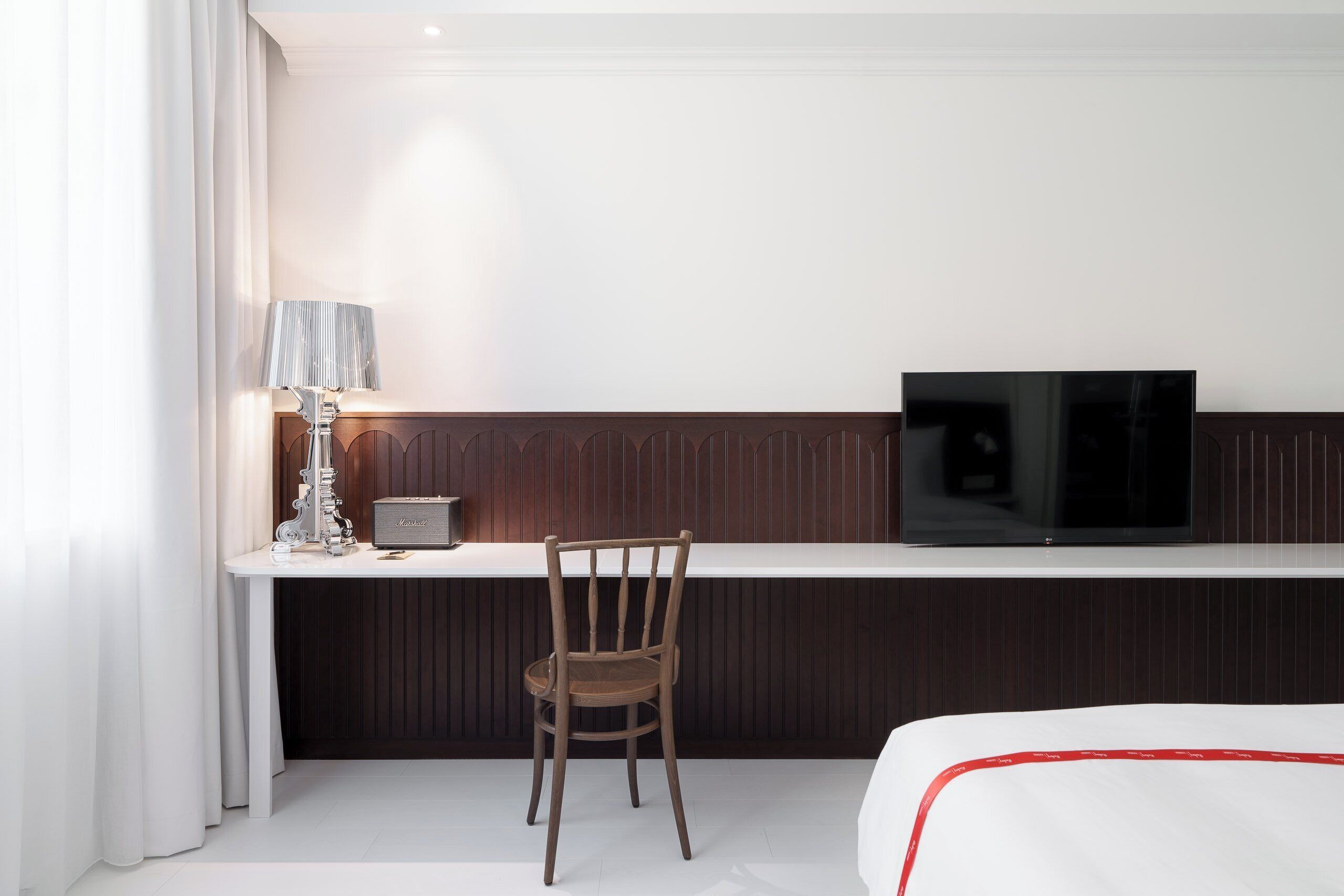 Ett hotellrum med en säng, ett skrivbord med en tv, en stol och en lampa.