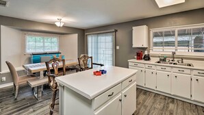 A modern kitchen with white cabinets, a central island, and a dining area with a table and chairs. - Copy of Copy Expedia (Converse)