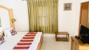 Quarto de hotel com uma cama, televisão, armário de madeira e janela com cortinas.