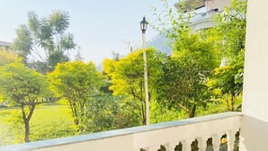 Un balcón con balaustrada blanca, mobiliario de mimbre y vistas a un paisaje verde.