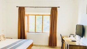 Un dormitorio con cama, escritorio, silla, televisor y ventana con cortinas.