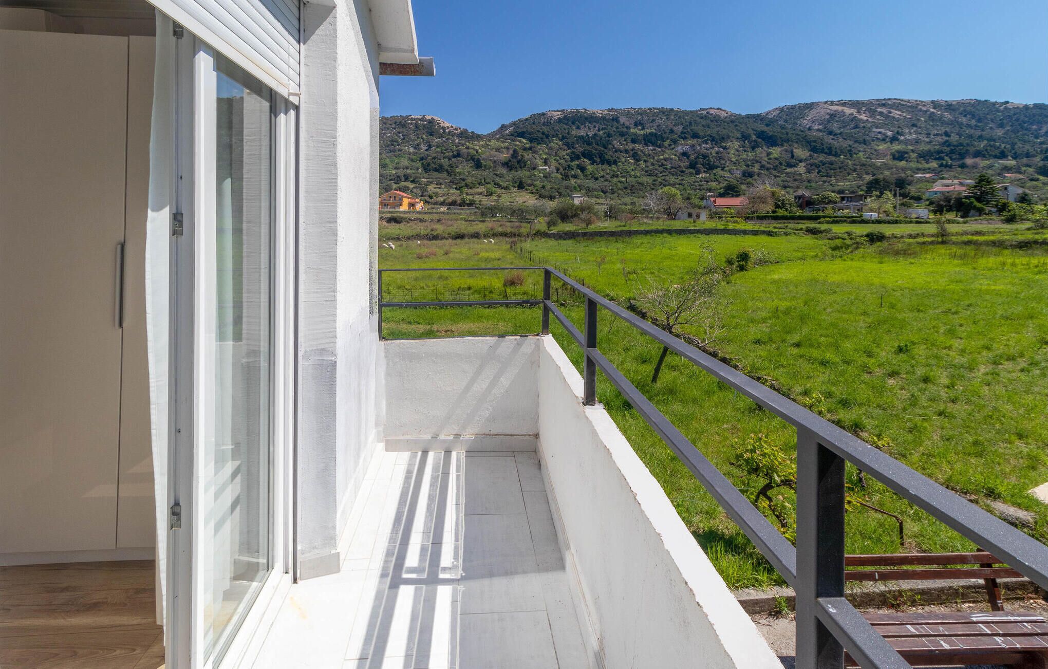 A balcony with a view of a green field and hills in the distance.