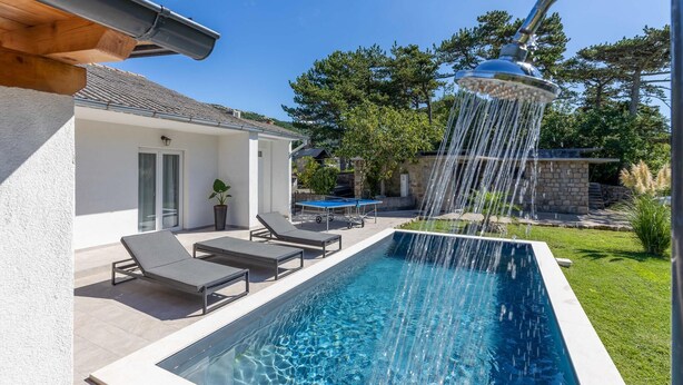 A swimming pool with a showerhead, lounge chairs, and a table.