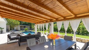 An outdoor patio with a pool, wooden ceiling, and a table with chairs.