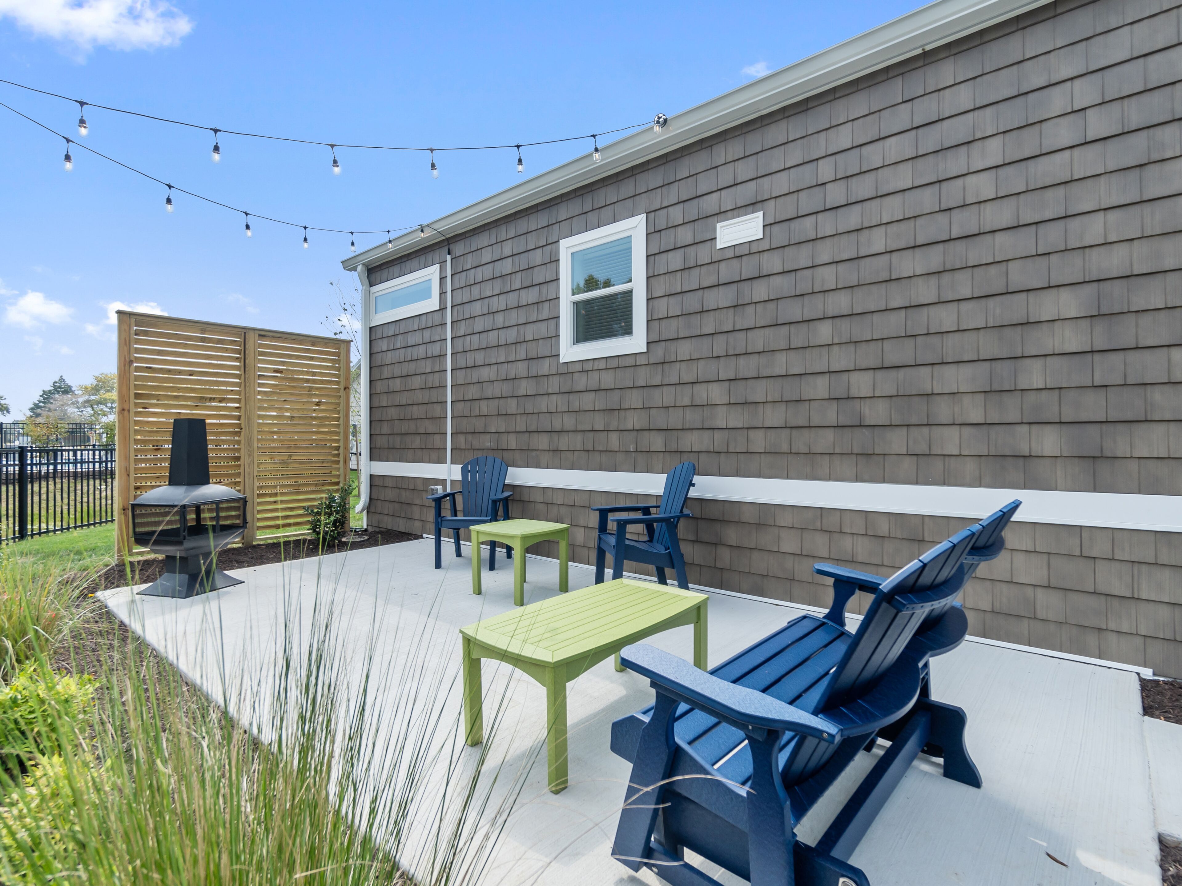 A patio area with outdoor furniture, a barbecue grill, and string lights against a house with siding.