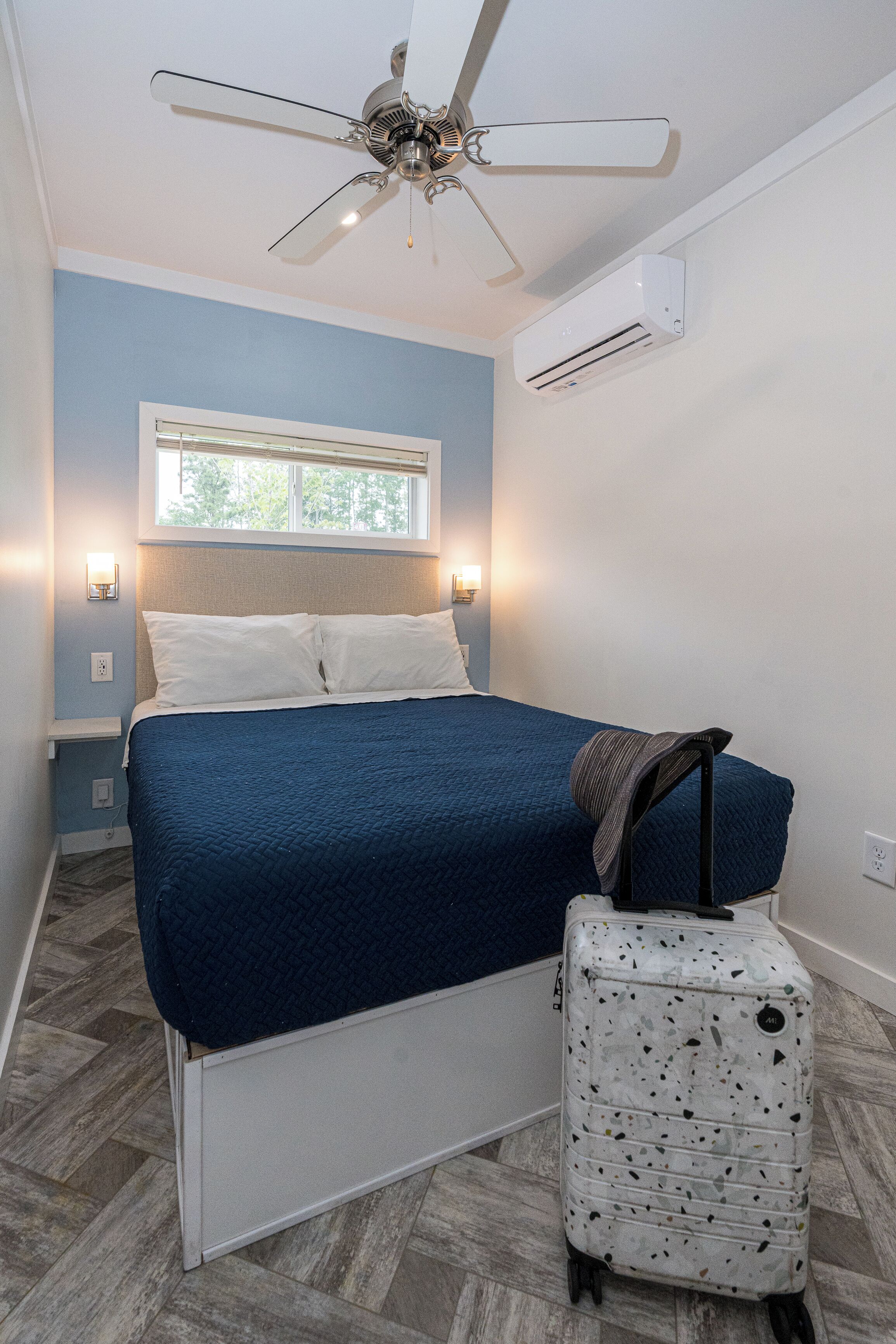 A bedroom with a bed, a ceiling fan, an air conditioning unit, and a suitcase.