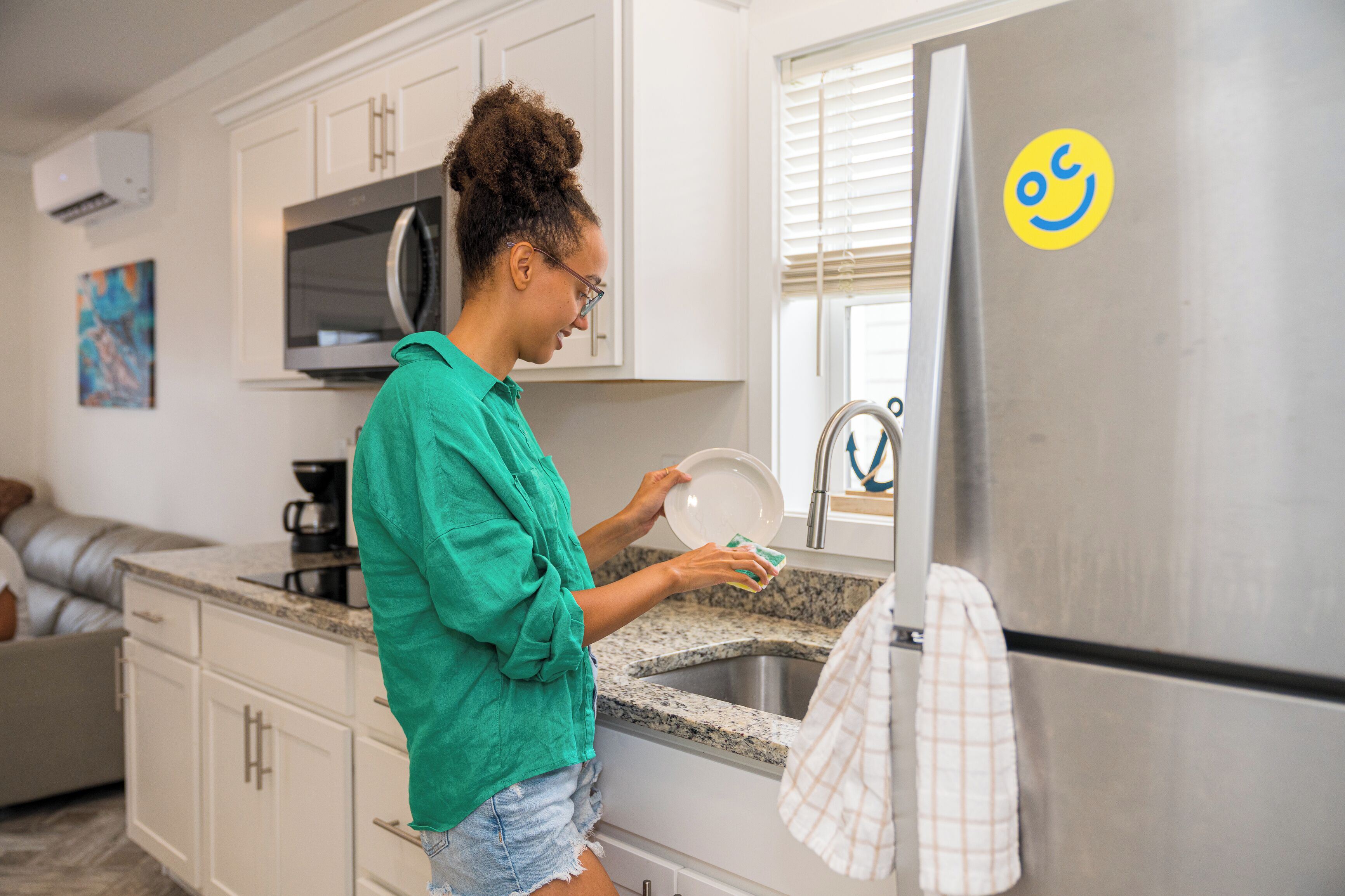 A kitchen with white cabinets, a stainless steel refrigerator, and a person washing dishes.