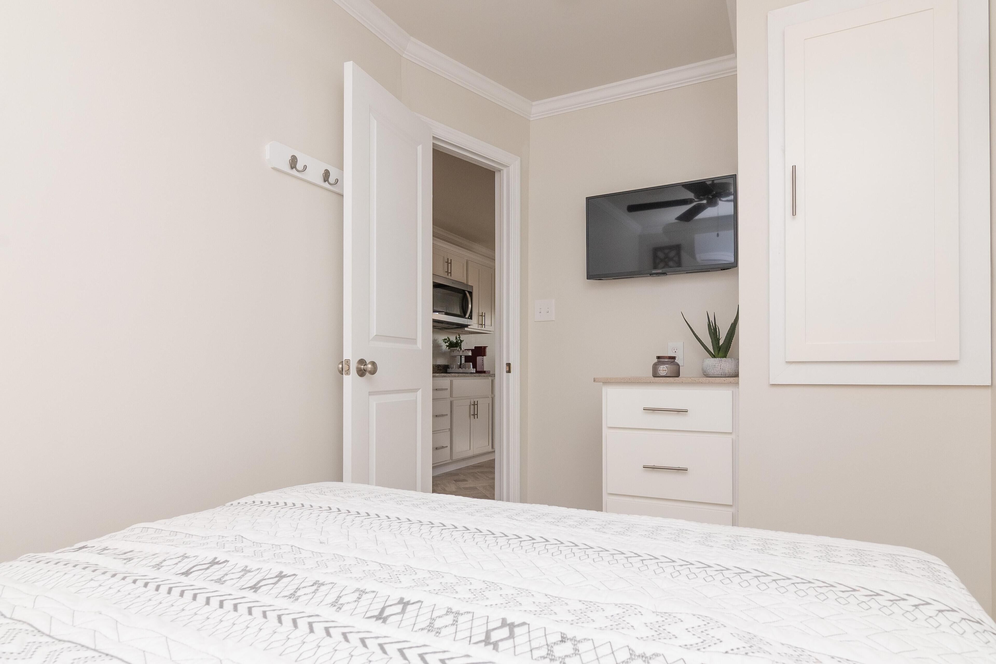A bedroom with a bed, a TV mounted on the wall, a wardrobe, and a door leading to a bathroom.