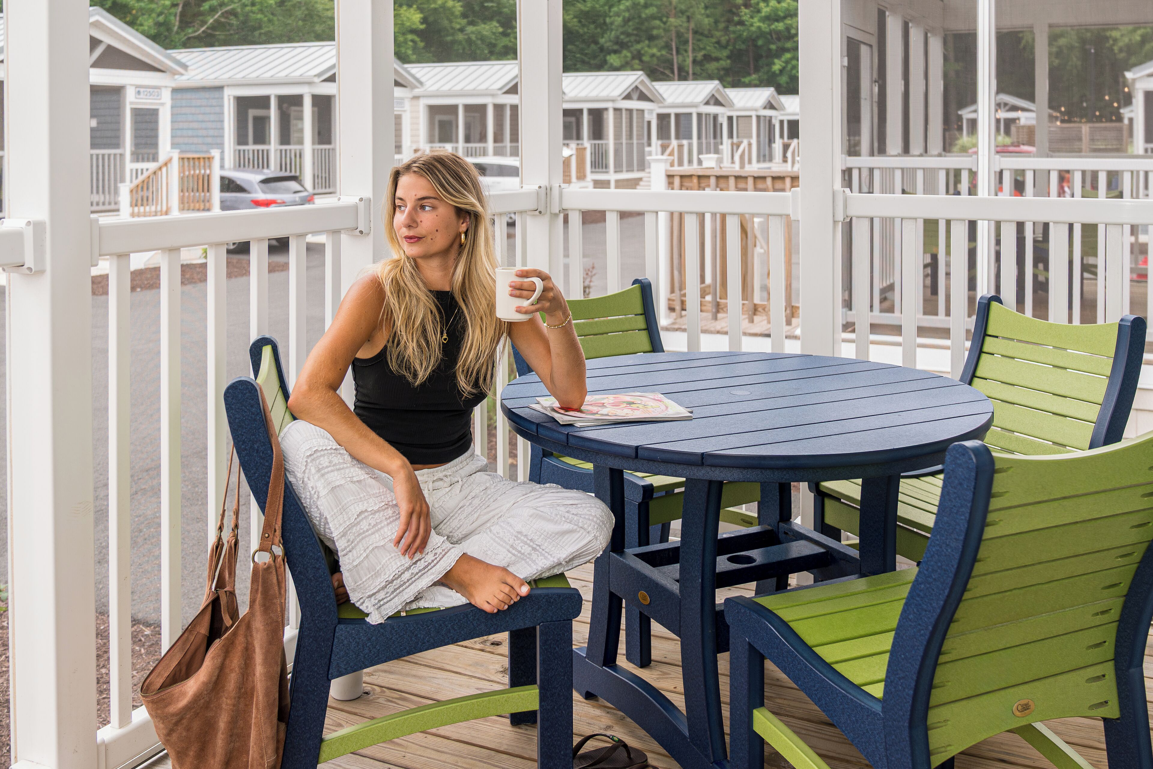 Iemand zit aan een ronde tafel met stoelen, op een houten terras met witte leuningen.
