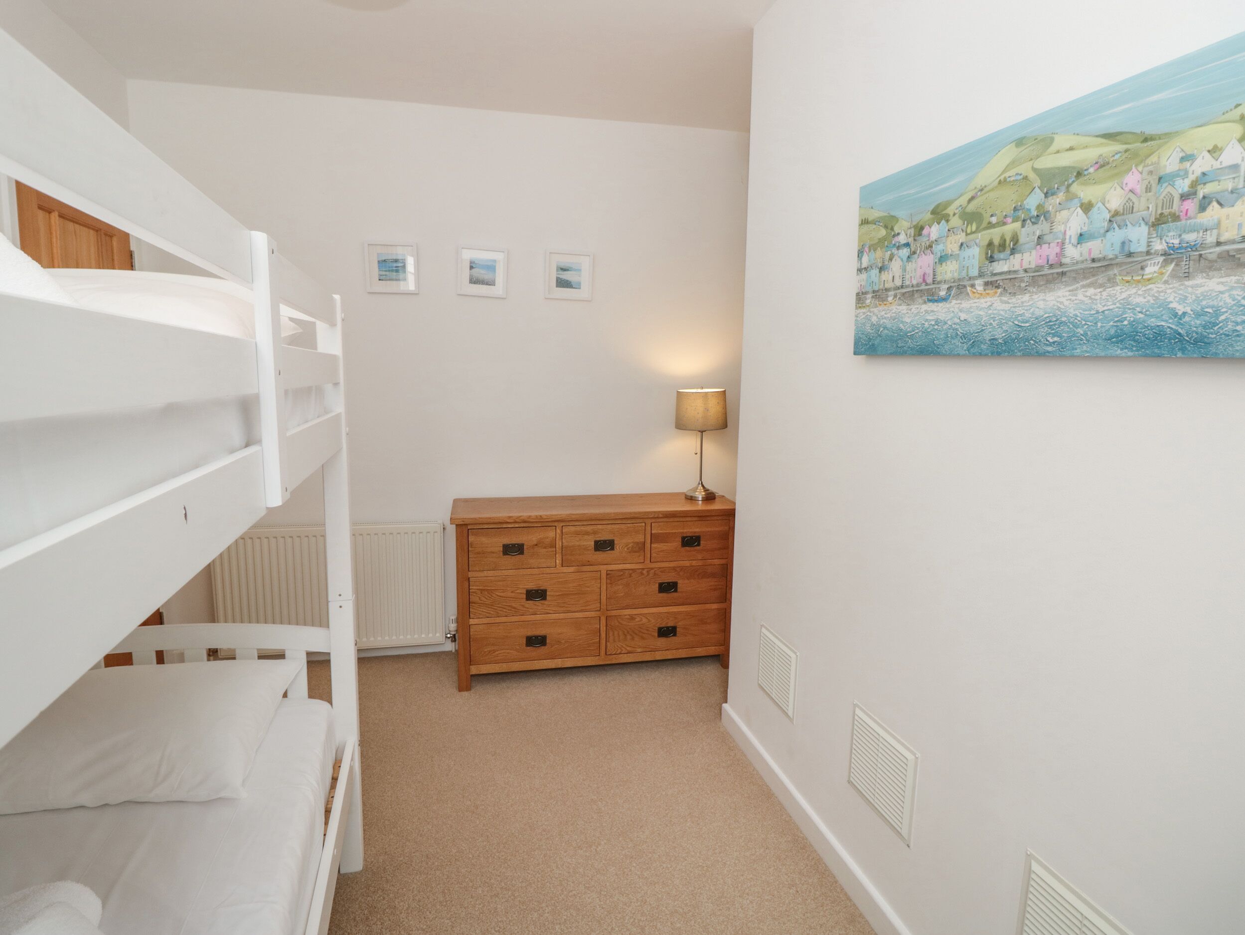 A bedroom with bunk beds, a dresser, a radiator, and a painting on the wall.