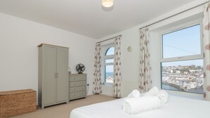 A bedroom with a bed, a wardrobe, a fan, a window with a view of a town, and a wicker basket. - 2 North Furzeham Road (Brixham)