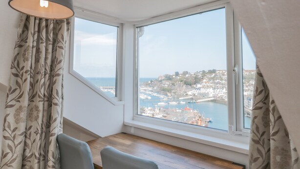 A room with a large bay window overlooking a harbor and town. - 2 North Furzeham Road (Brixham)