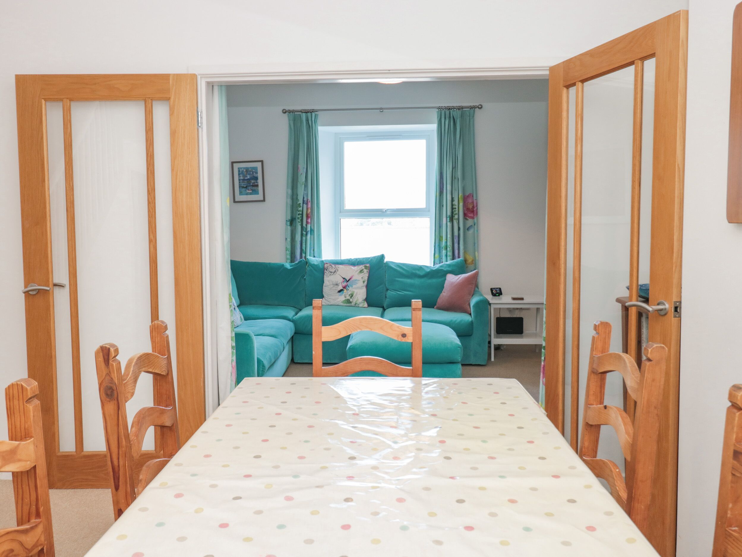 Une pièce comprenant une table à manger en bois, des chaises, un canapé de couleur turquoise et une fenêtre avec des rideaux.