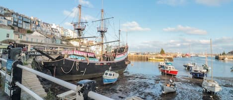 A harbor with a large sailing ship docked, surrounded by smaller boats and buildings along the waterfront.