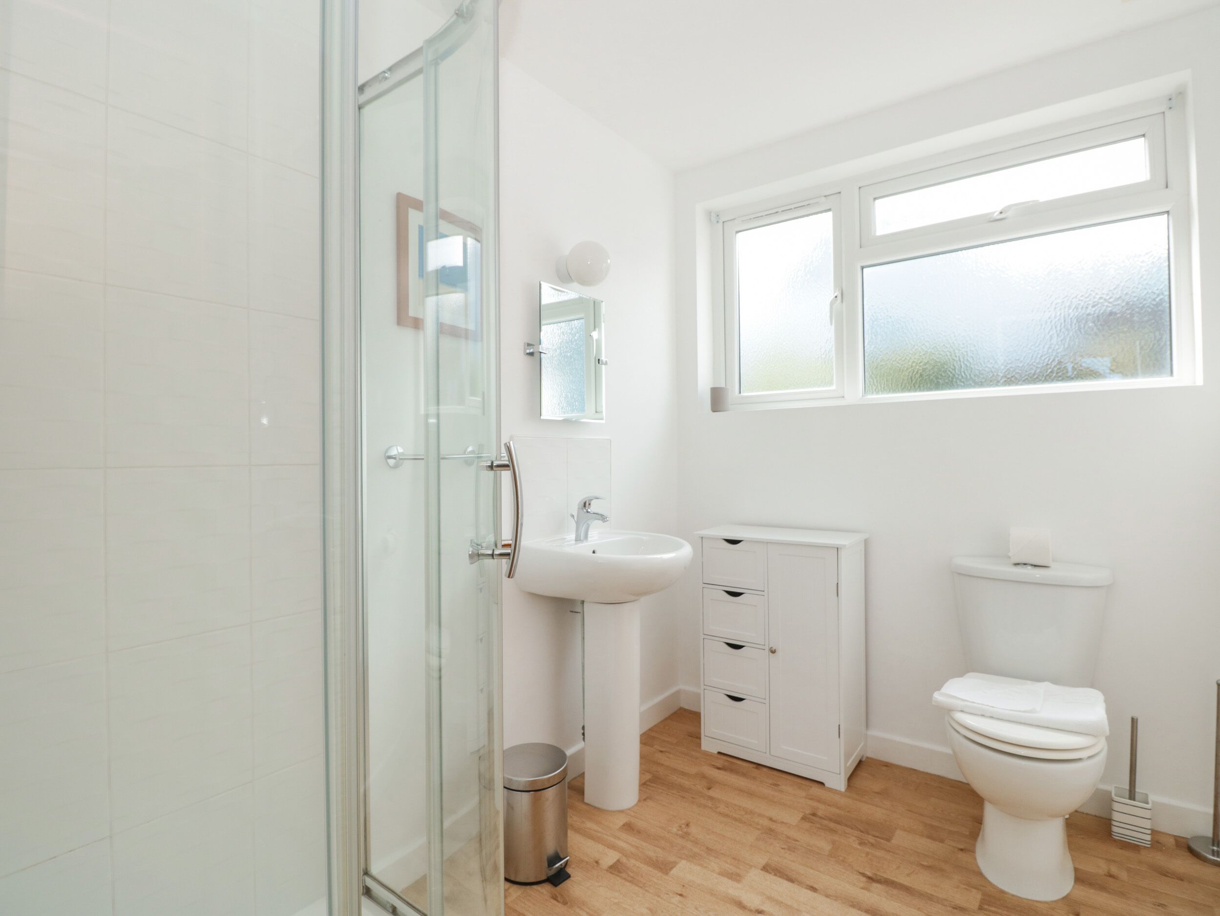 Ein Badezimmer mit Duschkabine aus Glas, einem weißen Waschbecken, einer Toilette und einem Schrank.