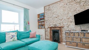 A living room with a teal sofa, a fireplace, a stone wall, a bookshelf, and a TV. - 2 North Furzeham Road (Brixham)