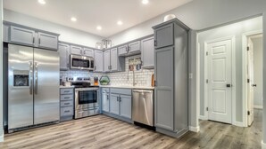 A modern kitchen with grey cabinets, stainless steel appliances, and a wooden floor.
