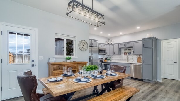 A modern kitchen with white cabinets, a wooden dining table set with plates and glasses, and a hanging light fixture.