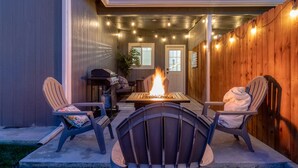 An outdoor patio with a fire pit, two Adirondack chairs, and a table.