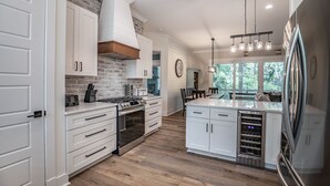 Een moderne keuken met witte kasten, een accentmuur van baksteen, roestvrijstalen apparatuur en een groot eiland met een geïntegreerde koelkast.