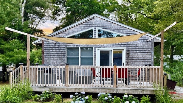 A house with a wooden deck, a covered porch, and a garden with hydrangea bushes. - Peaceful 3-Bedroom Beach Cottage with Deck, Beach Parking Pass & Outdoor Shower (South Kingstown)