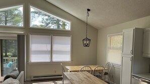 A compact kitchen with a wooden island, white cabinets, and a dining area with chairs. - Peaceful 3-Bedroom Beach Cottage with Deck, Beach Parking Pass & Outdoor Shower (South Kingstown)