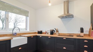 Une cuisine moderne avec des meubles de couleur sombre, une hotte de cuisinière en acier inoxydable, une fenêtre donnant sur la verdure et un plan de travail en bois.