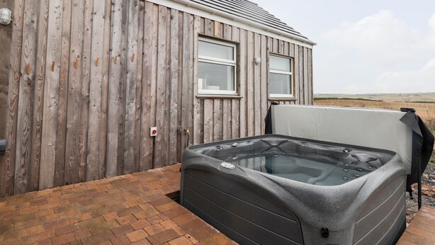 Une construction en bois avec deux fenêtres, une terrasse en briques et un jacuzzi.