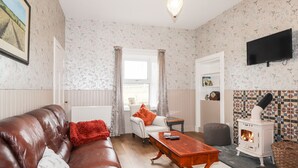 Un salon avec un canapé en cuir marron, une table basse en bois, un radiateur blanc, une cheminée et un téléviseur fixé au mur.