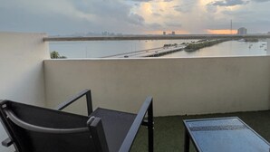Un balcon offrant une vue sur une étendue d’eau, les contours d’une ville lointaine et un ciel nuageux.