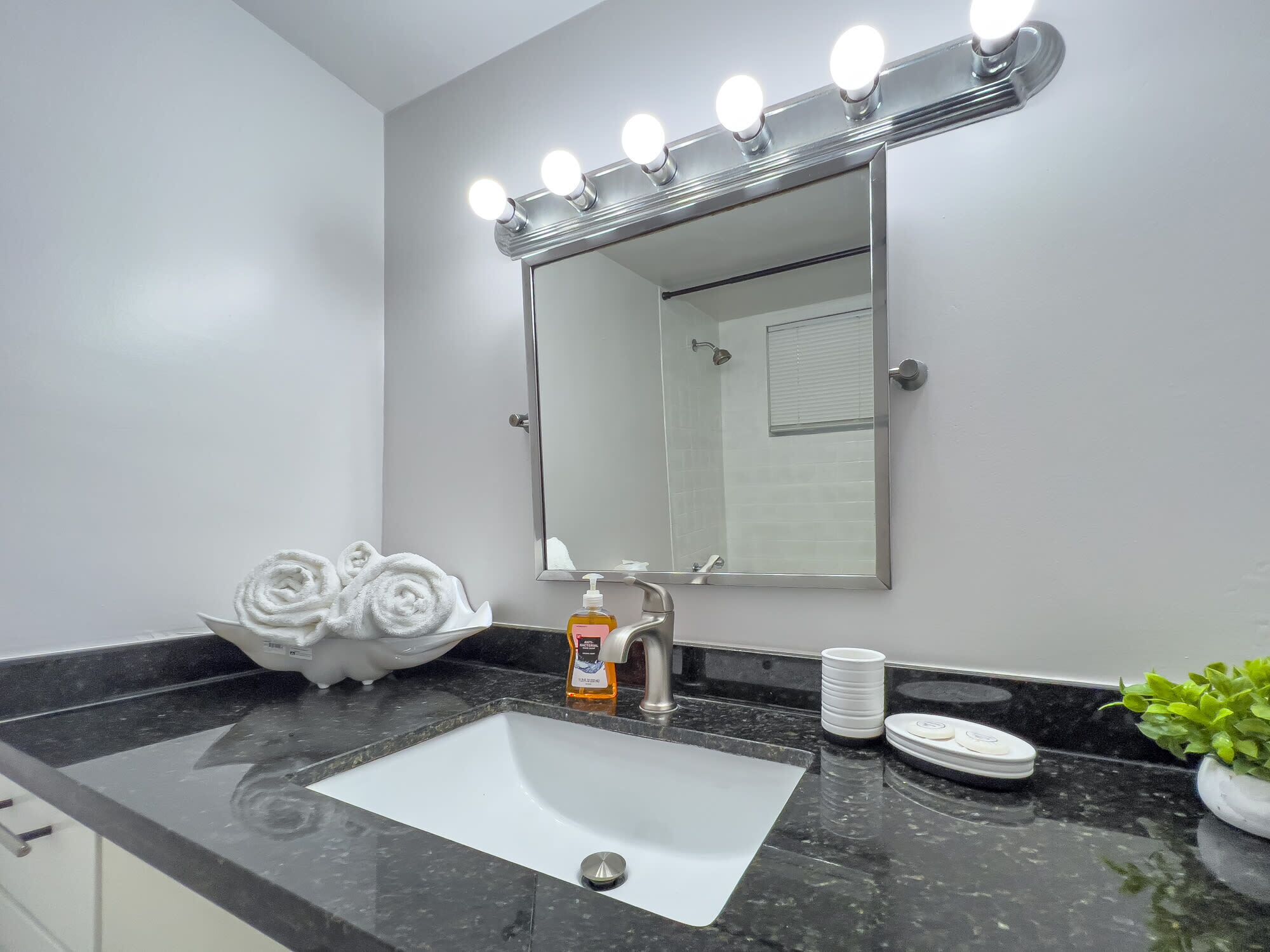 A bathroom with a sink, mirror, towel rack, soap dispenser, and a scale.