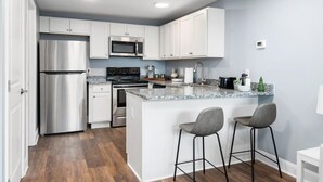 A modern kitchen with white cabinets, stainless steel appliances, a granite countertop, and two bar stools. - Newly Renovated 1 Bedroom (Columbus)