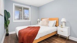 A bedroom with a bed, bedside tables, a window, and a potted plant. - Newly Renovated 1 Bedroom (Columbus)