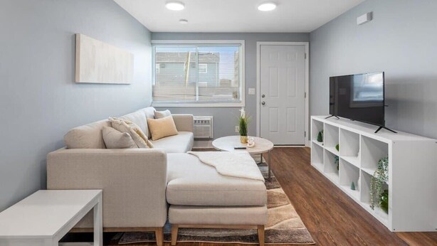 A modern living room with a sofa, ottoman, white shelving unit, and a TV. - Newly Renovated 1 Bedroom (Columbus)