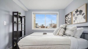 A bedroom with a bed, a window, a bookshelf, and two wall-mounted flower paintings.
